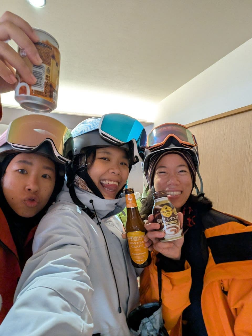 Three women in helmets and goggles toasting with drinks after a day on the slopes
